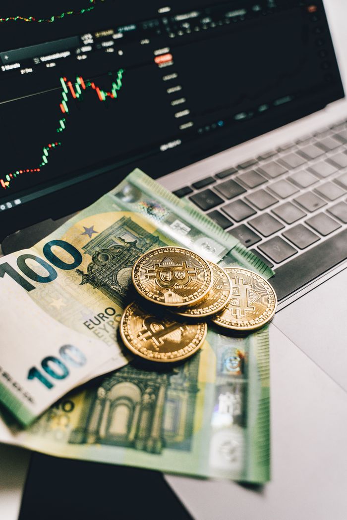 Euro banknotes and Bitcoin coins on a laptop, showcasing finance and cryptocurrency trends.